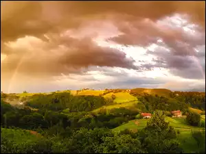 Kolorowa tęcza nad wzgórzami porośniętymi drzewami i domami