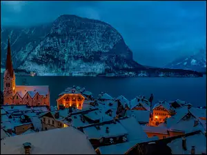 Austriackie miasto Hallstatt zimą z kościołem i oświetlonymi domami na tle gór