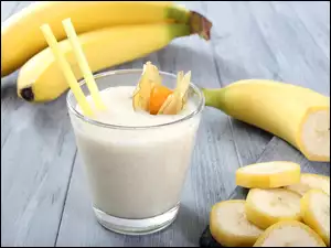 Koktajl bananowy w szklance obok pokrojonego banana na desce