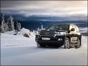 Czarna Toyota Land Cruiser na tle ośnieżonych drzew i szczytów gór