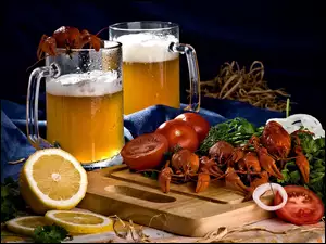na desce ułożone raki z pomidorami i przekrojoną cytryną oraz kufle piwa z pianką