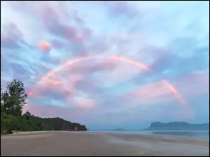 Morska plaża z drzewami i tęczą na niebie