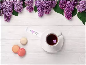 Bez ułożony na deskach obok filiżanki z kawą i makaroników
