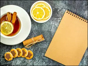 Notes położony obok ciasteczek i filiżanki z herbatą