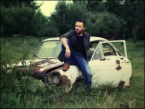 Facet siedzący na masce starego samochodu