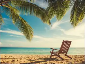 Drewniany leżakpod liśćmi palmy na morskiej plaży