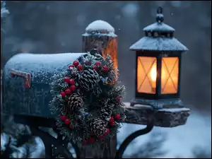 Ośnieżona latarnia i wieniec świąteczny na skrzynce pocztowej obok choinki w zimowej scenerii