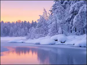 Śniegowe zaspy i ośnieżone drzewa na brzegu rzeki