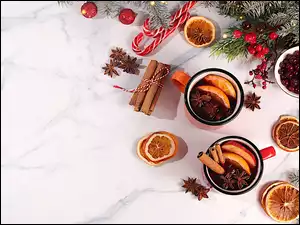 Na blacie kubki z grzanym winem i przyprawami oraz suszonymi owocami pomarańczy