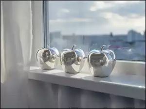 Trzy srebrne jabłka w słońcu na parapecie okna obok jasnej zasłonki