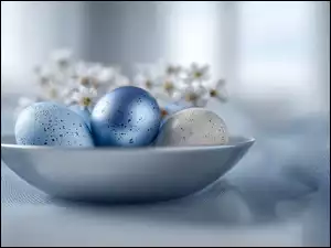 Trzy kolorowe jajka w kropkiw jasnoniebieskiej misce