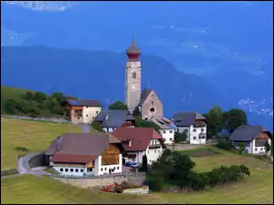Kościół i domy na wzgórzu na tle zalesionych gór