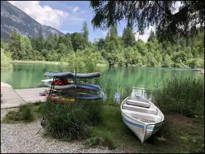 Deski surfingowe i łódka na brzegu jeziora przy pomoście