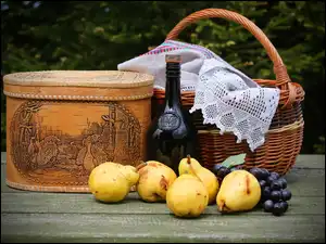 Gruszki i winogrona obok koszyka i butelki z winem