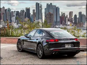 Porsche Panamera Turbo na parkingu przy ogrodzeniu z widokiem na drapacze chmur