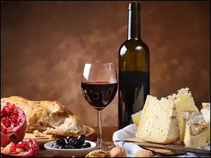 Czerwone wino w kieliszku i butelce obok sera granatu i pieczywa